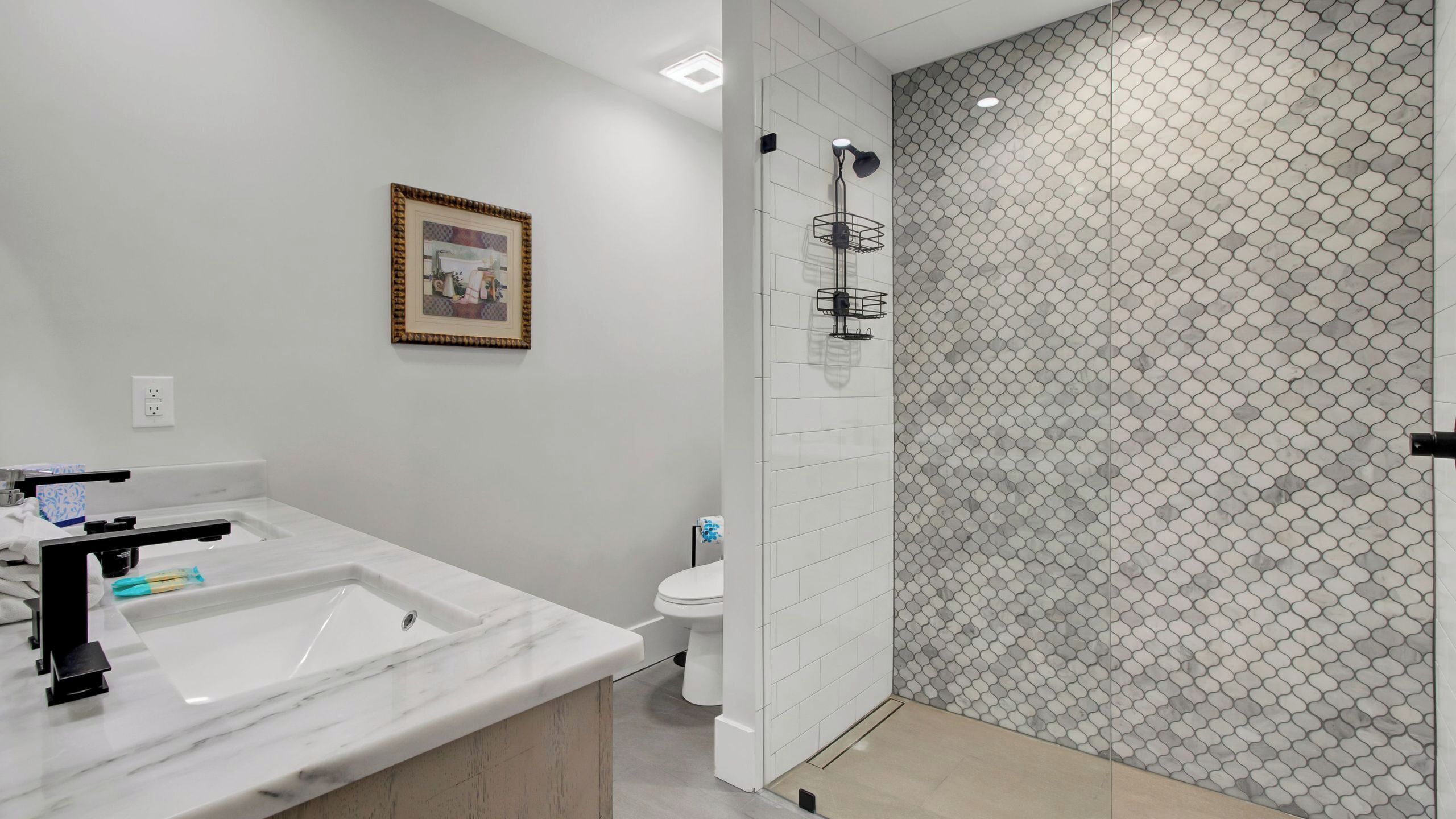 Een moderne badkamer met een marmeren wastafel, toilet en douchegedeelte met een honingraatmotief.