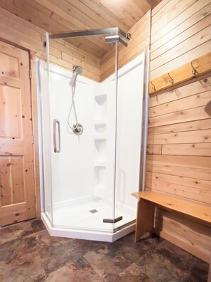 A corner shower room with a glass door, wooden walls, and a bench. - Sleeping Bear Resort (Lake Ann)