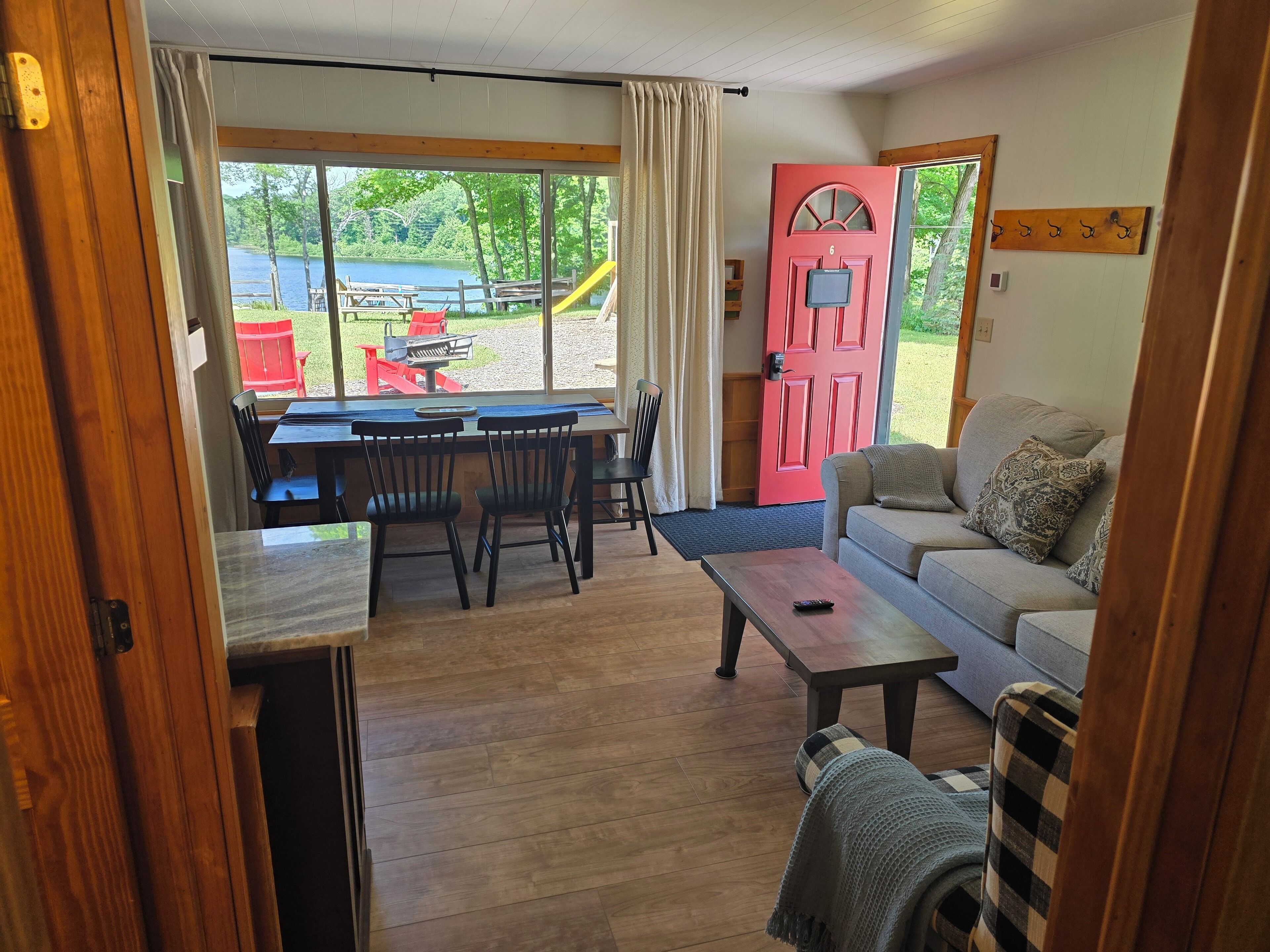 A cozy room with a wooden floor, a sofa, a dining table with chairs, and a red door.
