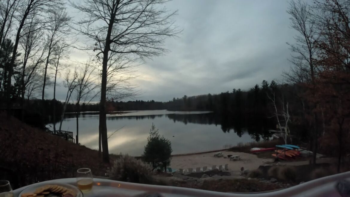 A lakeside view with a dining table and chairs, a glass of beer, and a plate of food.
