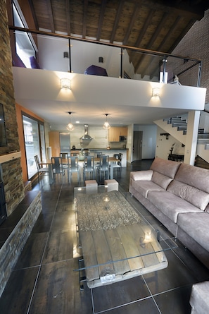 A spacious living area with a high ceiling, a sofa, a glass coffee table, and a kitchen in the background. - Country House 'La Puerta Del Rio Lobos' with Mountain View, Private Pool and Wi-Fi (San Leonardo de Yagüe)
