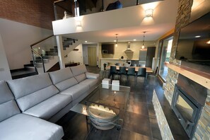 A modern living room with a sofa, a glass coffee table, a fireplace, and a kitchen in the background. - Country House 'La Puerta Del Rio Lobos' with Mountain View, Private Pool and Wi-Fi (San Leonardo de Yagüe)