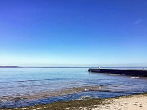 En kustvy med en klar himmel, stilla vatten och en sandstrand.