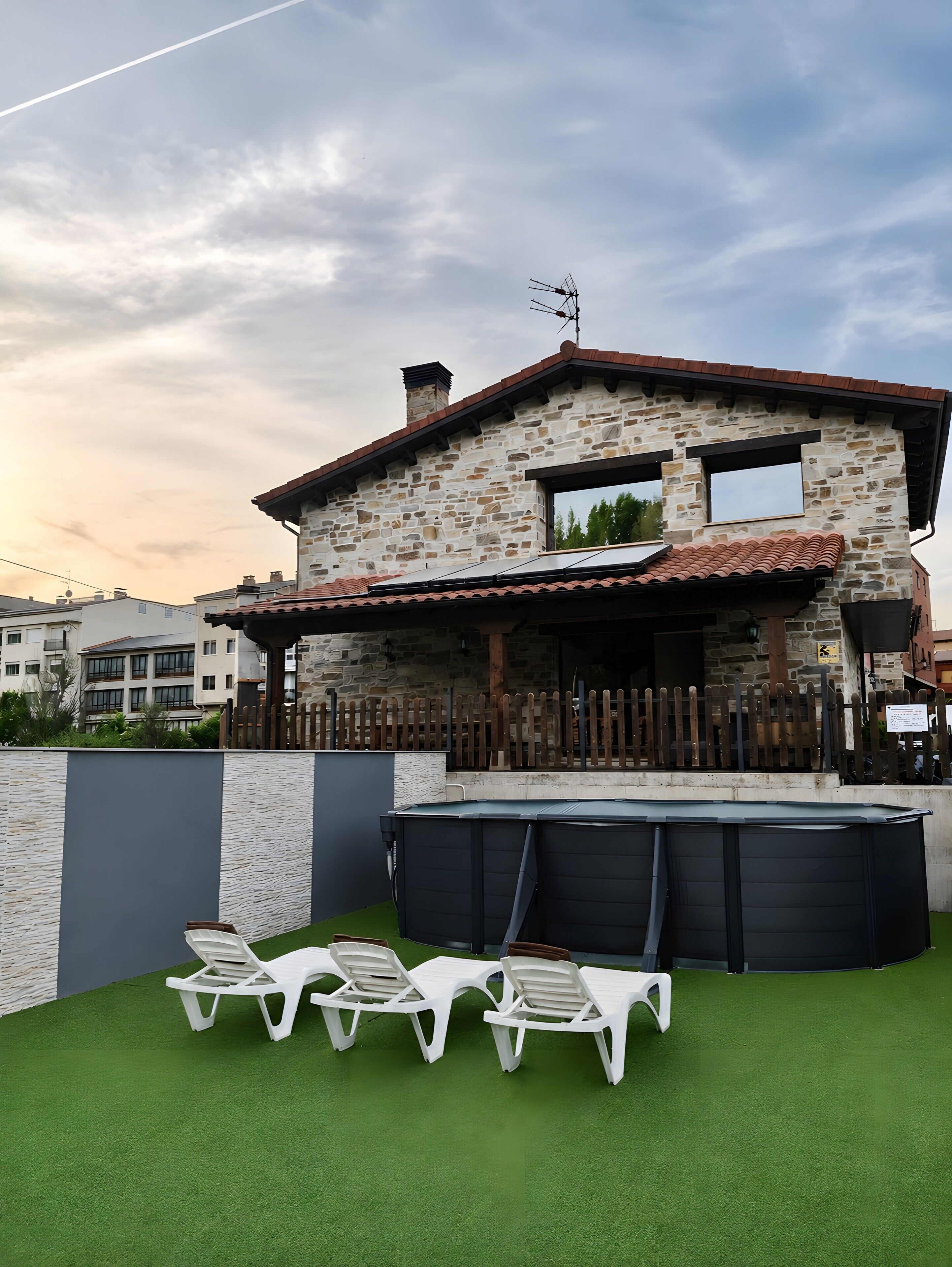 A stone house with a swimming pool and lounge chairs.