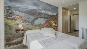 Un dormitorio con una cama grande, una mesita de noche con lámpara y un mural en la pared de un paisaje montañoso.