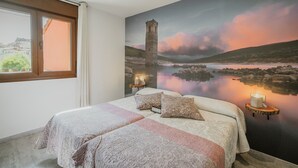 Un dormitorio con una cama grande, una ventana, un mural de una torre y una mesita de noche con una vela.
