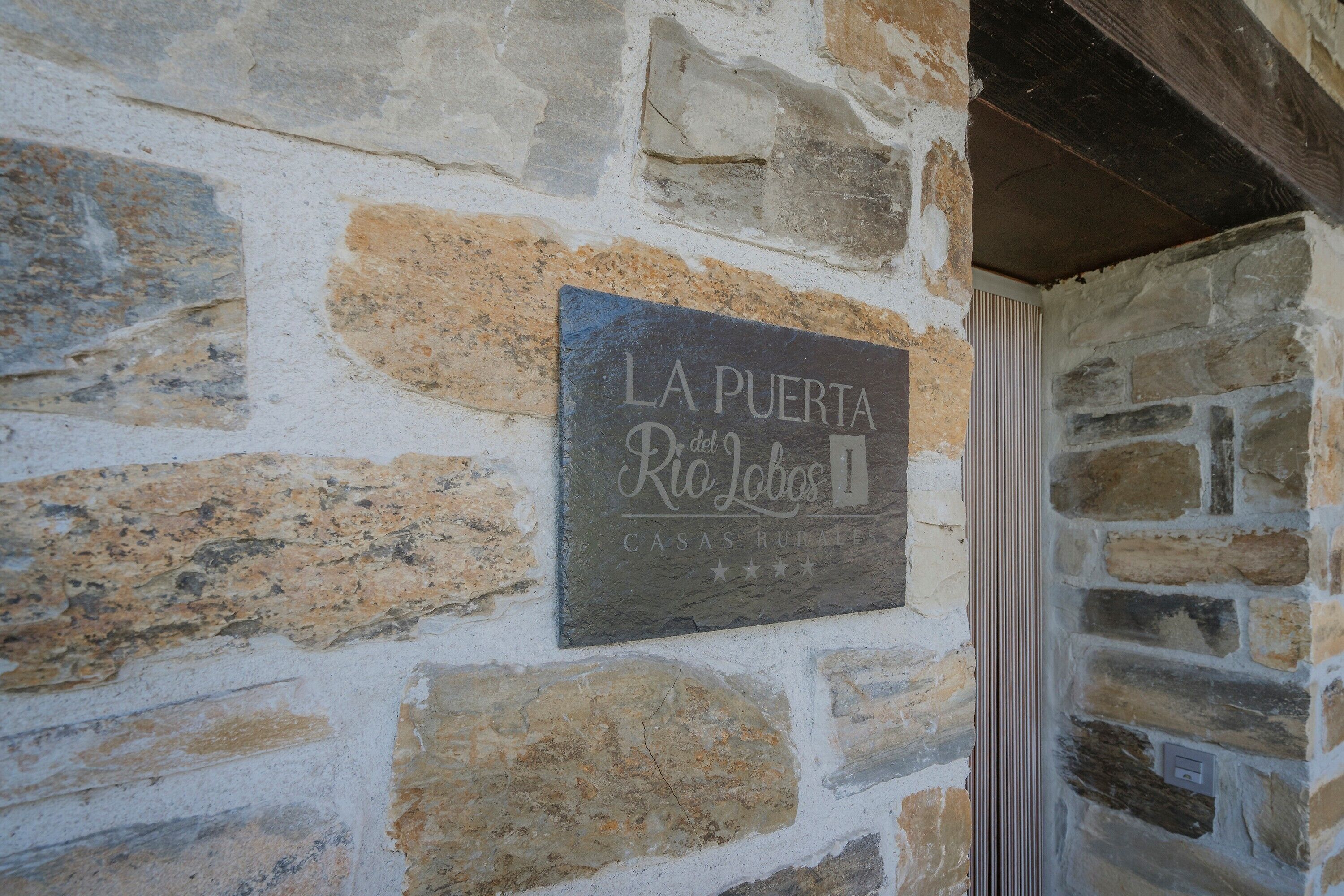 Un muro de piedra con un cartel que dice 'LA PUERTA del Rio Lobos Casas Rurales'.