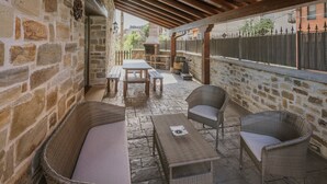 A stone-walled patio with wicker furniture, a wooden table, and a barbecue area. - Country House 'La Puerta Del Río Lobos I' with Private Pool, Shared Terrace and Wi-Fi (San Leonardo de Yagüe)