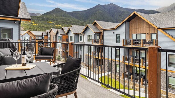 Eine Terrasse mit Gartenmöbeln, einem Tisch mit einer Weinflasche und Blick auf Berghütten.