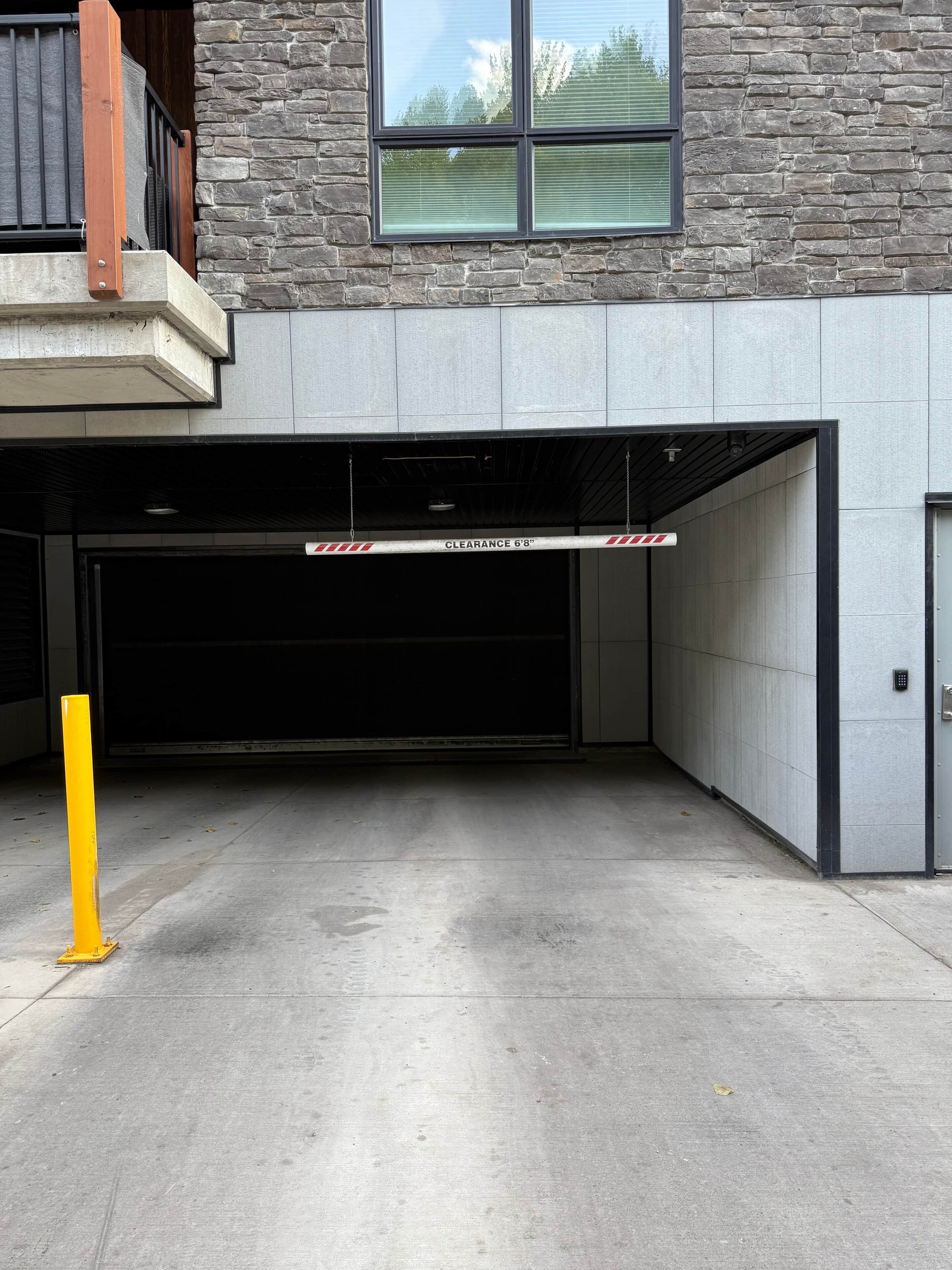 A parking garage entrance with a clearance sign, a yellow bollard, and a stone facade.