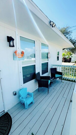 Un portico coperto con rivestimento bianco, due finestre con pannelli vista, un tavolino e due sedie, una poltrona Adirondack blu e un lanterna nera.
