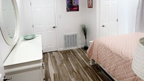 A bedroom with a wooden floor, a bed with a pink blanket, a white dresser, a mirror, and a door. - Tequila Time in Rockport, TX (Rockport)