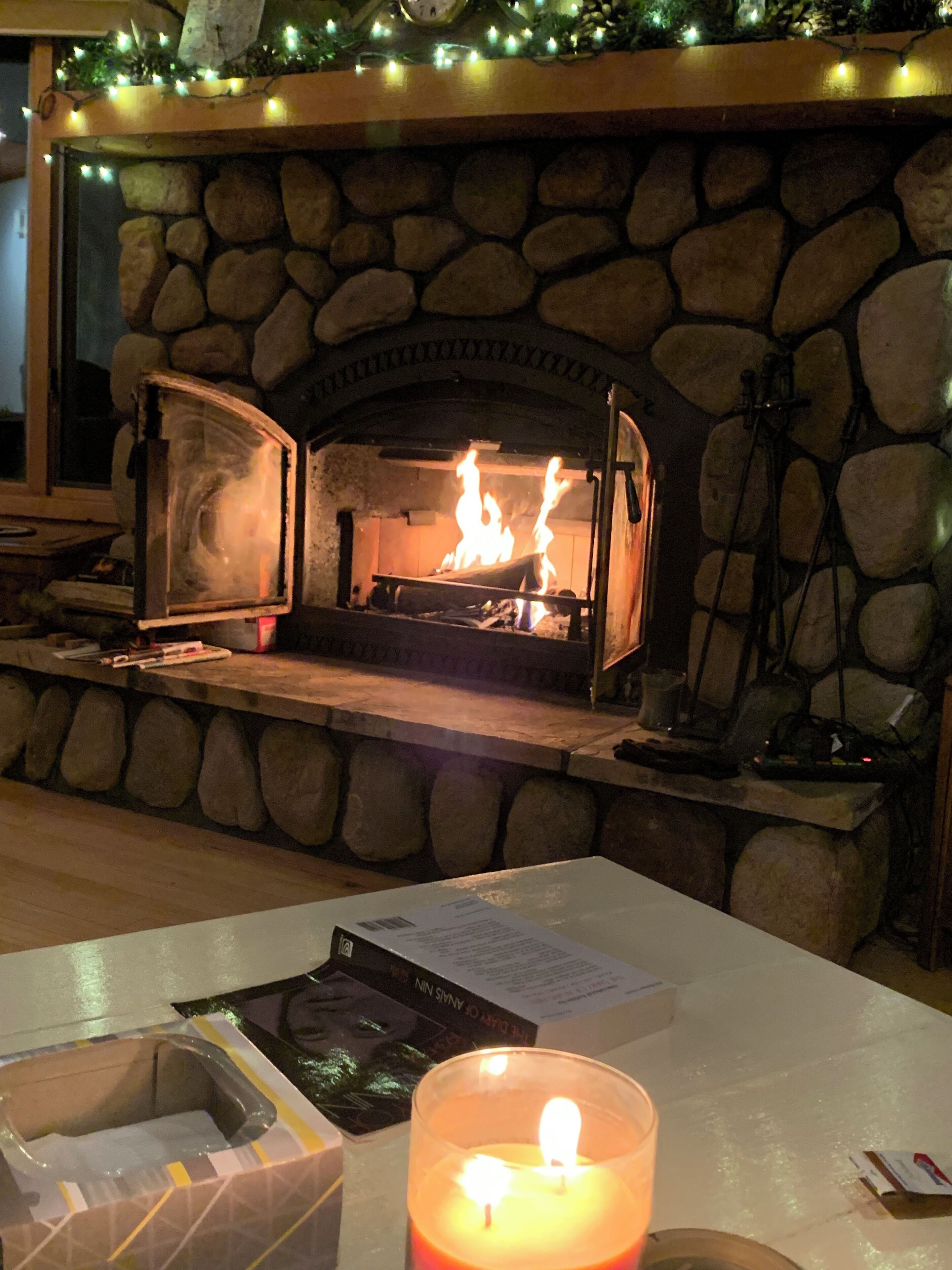 A stone fireplace with a fire, a table with a candle, and a book.