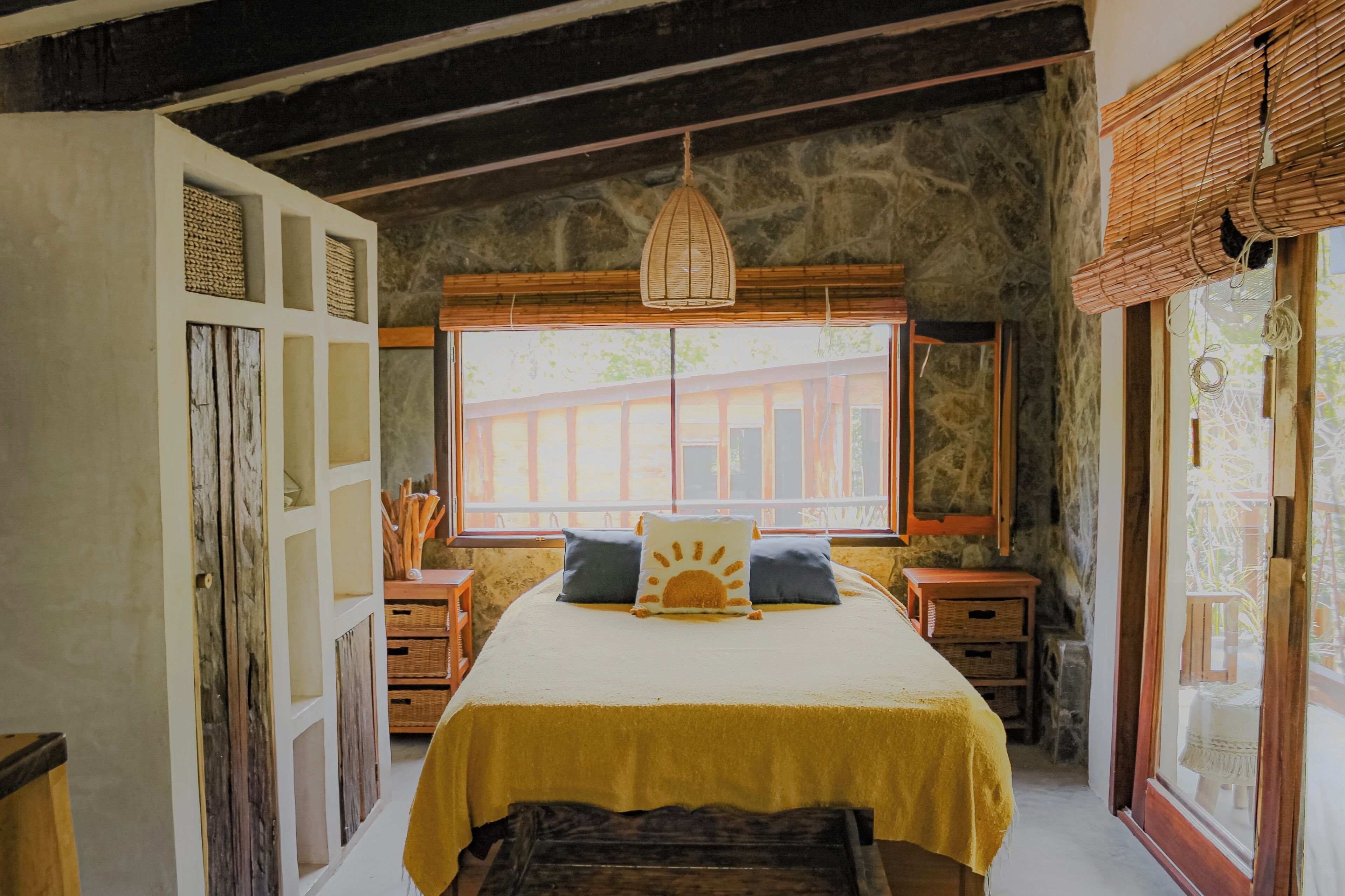 Una camera da letto con parete in pietra, un'ampia finestra, un letto con copripiumino giallo e una lampada a sospensione.