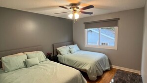Un dormitorio con dos camas, un ventilador de techo, una ventana y una pequeña mesa.