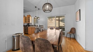 Una cocina moderna con armarios de madera, una mesa de comedor y sillas. Hay un bote de basura y una lámpara colgante.
