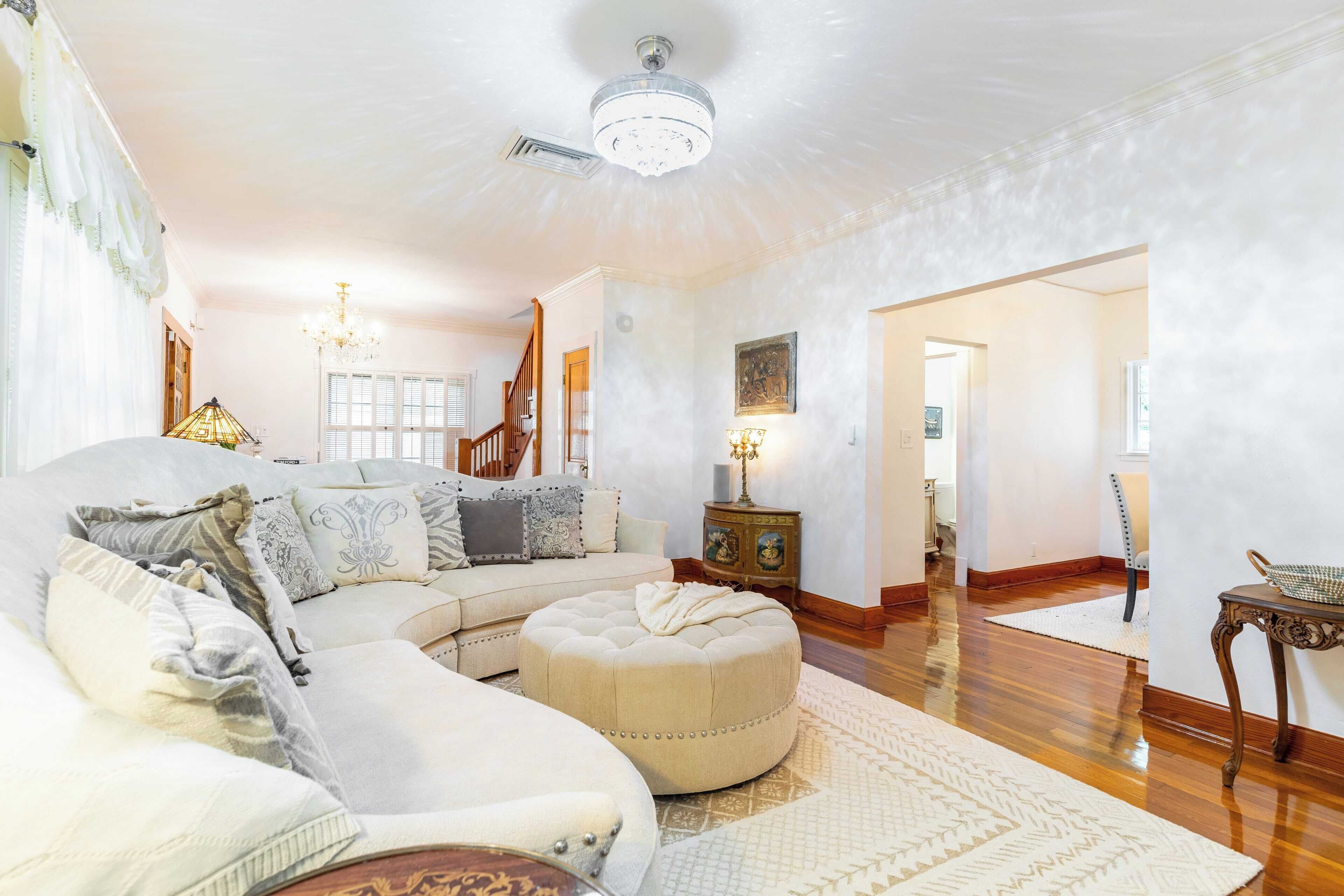 A spacious living room with a large sectional sofa, a round ottoman, and a chandelier.