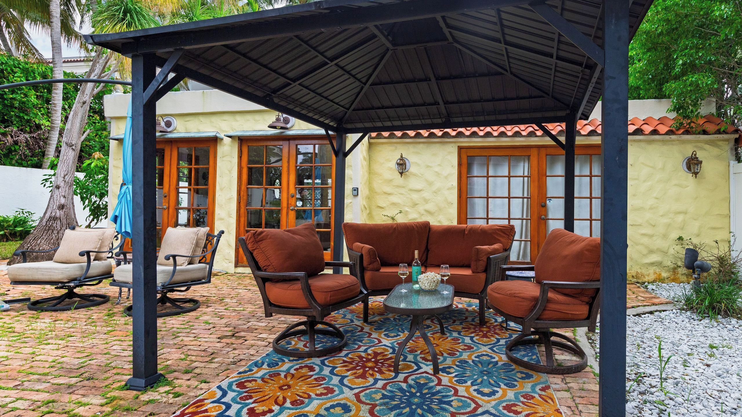 A covered patio with outdoor furniture, a patterned rug, and a view of a building with large windows and doors.