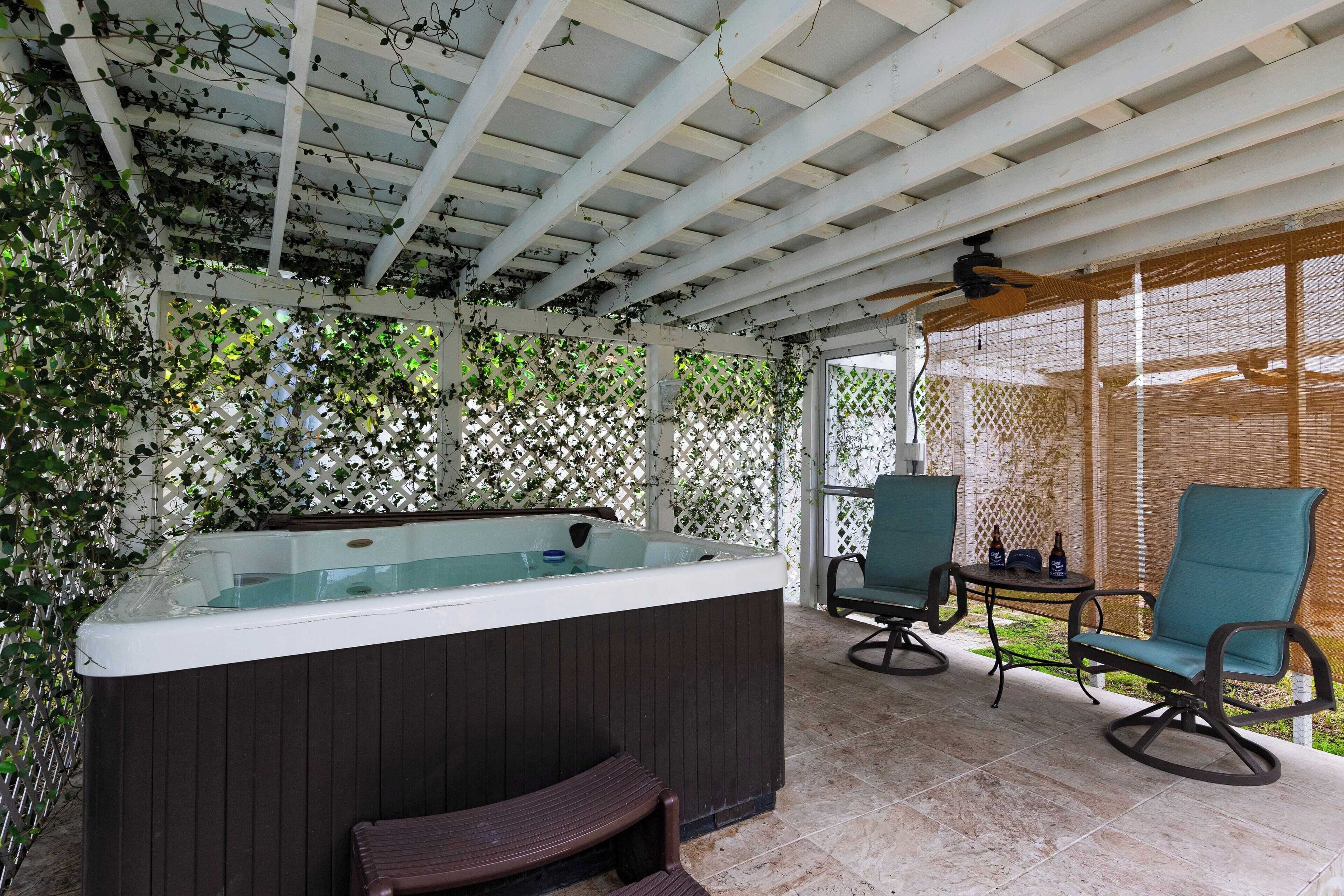 A covered outdoor area with a hot tub, two rocking chairs, and a table with bottles.