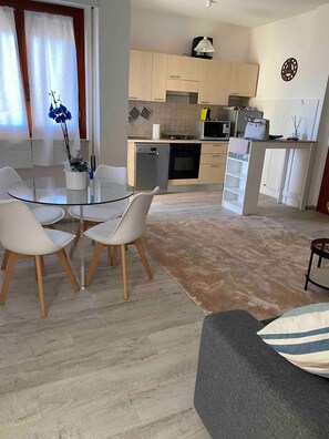 Une cuisine moderne avec des meubles en bois, un coin repas doté d’une table en verre et un espace de vie avec un canapé.