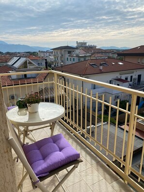 A balcony with a table, a purple cushion, and a potted plant. - Apartment 'Fronte Mare' with Balcony, Wi-Fi and Air Conditioning (Camaiore)