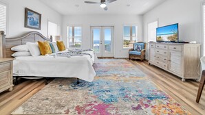 A spacious bedroom with a large bed, a ceiling fan, a television, and a view of the outdoors.