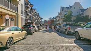A cobblestone street lined with multi-story buildings, parked cars, and pedestrians.