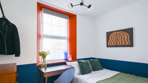 A bedroom with a bed, a desk, a chair, a window, and a ceiling fan.