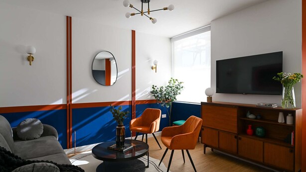 A modern living room with a sofa, two orange chairs, a round coffee table, a TV, and a wooden cabinet.