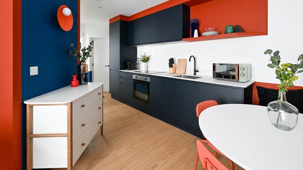 Een moderne keuken met een wit aanrecht, zwarte kastjes en een rode accentmuur.