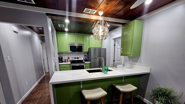 Una cocina con armarios verdes, una encimera blanca y dos taburetes de bar.