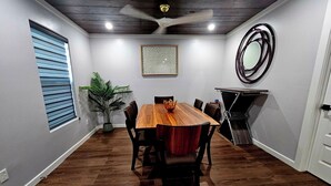 Un salón de conferencias con una mesa de madera, sillas, un ventilador de techo, una planta en maceta y un espejo montado en la pared.