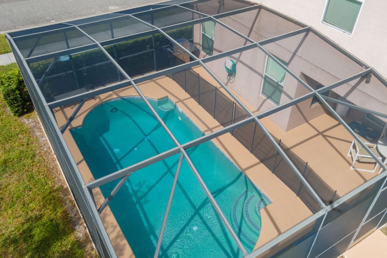 Une piscine dotée d’une enceinte en verre, entourée d’un patio aménagé avec une chaise et un tuyau d’arrosage.