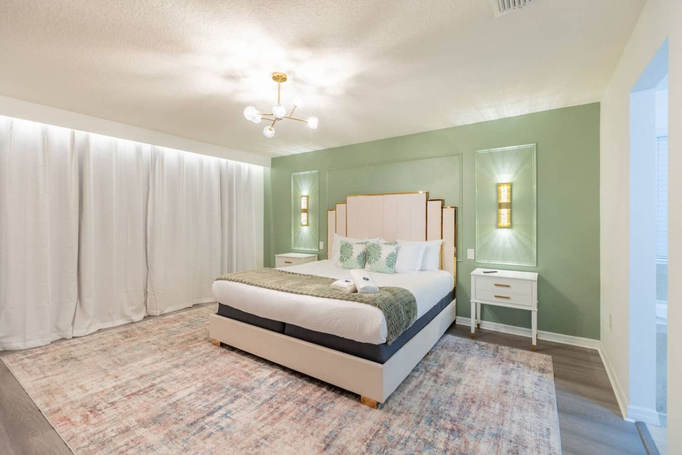A bedroom with a bed, nightstands, a chandelier, and a view of the outside.