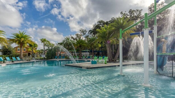 A clear blue pool with a water feature, surrounded by palm trees and lounge chairs. - Cozy 4br House w/ EV Charger & Perfect Location! (Kissimmee)