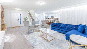 A modern living room with a blue sofa, grey armchairs, and a white coffee table. - Cozy 4br House w/ EV Charger & Perfect Location! (Kissimmee)