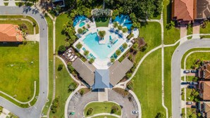 An aerial view of a residential area with a central swimming pool, multiple houses, and a roundabout. - Cozy 4br House w/ EV Charger & Perfect Location! (Kissimmee)