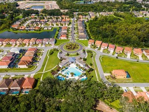 An aerial view of a residential area with a central roundabout, houses, and a swimming pool. - Cozy 4br House w/ EV Charger & Perfect Location! (Kissimmee)