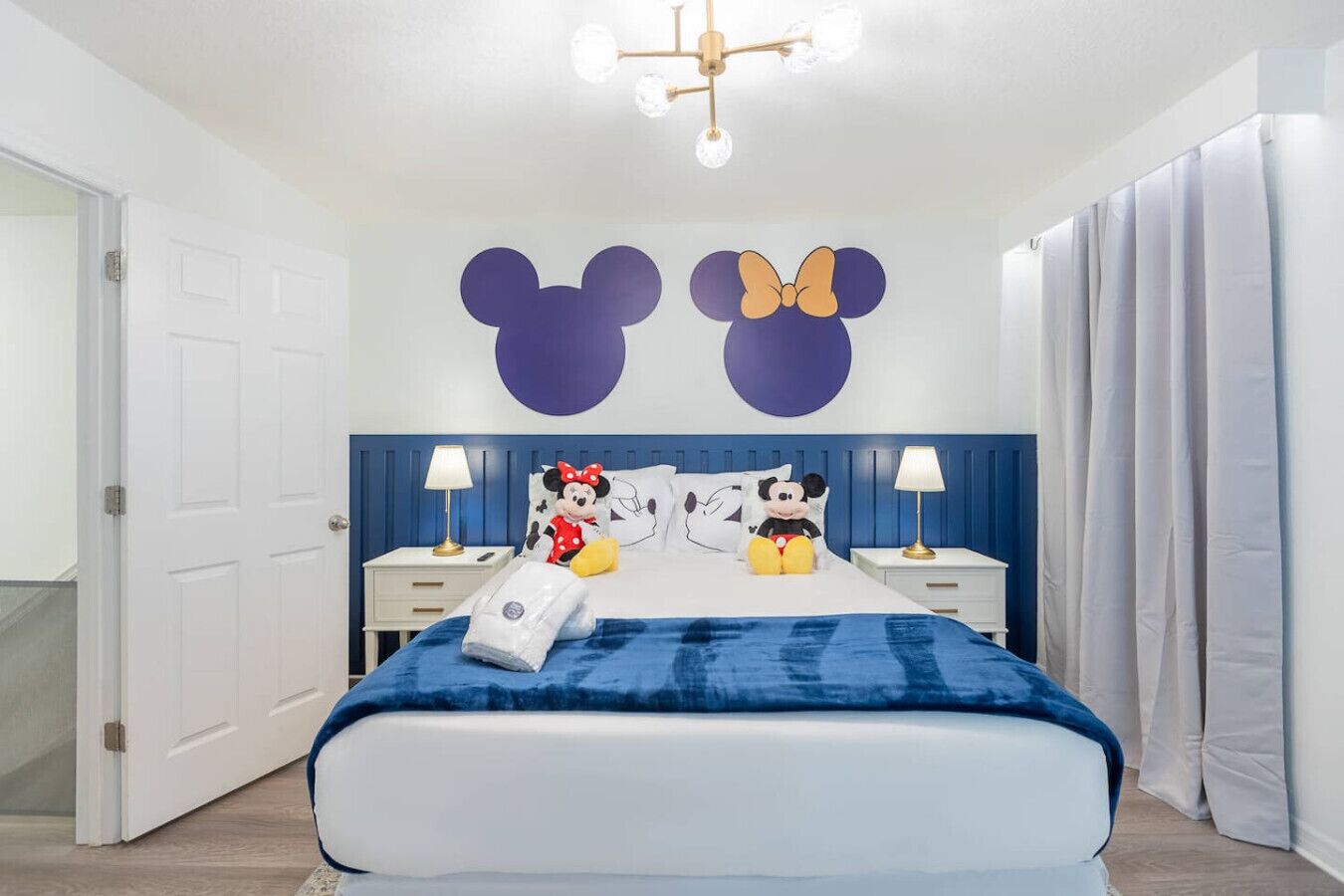 Quarto com cama, duas mesas de cabeceira, um enfeite de parede do Mickey Mouse e um travesseiro do Mickey Mouse.