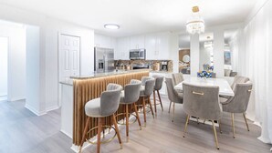 A modern kitchen with a central island, bar stools, and a dining table with chairs. - Cozy 4br House w/ EV Charger & Perfect Location! (Kissimmee)