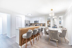 A modern kitchen with a central island, bar stools, and a dining table with chairs. - Cozy 4br House w/ EV Charger & Perfect Location! (Kissimmee)