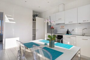 Una cocina moderna con armarios blancos, una mesa de comedor con sillas transparentes y una orquídea en maceta sobre la mesa.