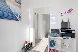 Una camera d'albergo moderna con pavimento in legno, una scrivania con stampante, un vaso con fiori e un quadro appeso al muro.