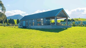 Un edificio moderno con un amplio ventanal, un patio cubierto y un campo de césped al frente.