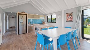 Una cocina moderna con una isla central, una zona de comedor con sillas azules y un amplio ventanal con vistas al exterior.