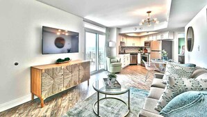 A modern living room with a large TV, a wooden console, a sofa set, and a dining area with a table and chairs. - Beach SPECIAL BayView Resort, 1 Bedroom Suite (Myrtle Beach)
