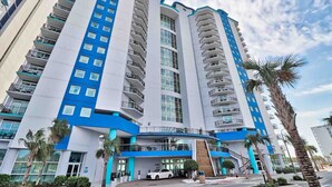 A multi-story hotel with balconies, a parking area, and palm trees. - Beach SPECIAL BayView Resort, 1 Bedroom Suite (Myrtle Beach)
