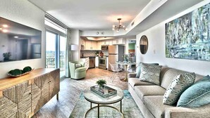 A modern living room with a sofa, coffee table, and TV. There is a kitchen in the background with cabinets and appliances. - Beach SPECIAL BayView Resort, 1 Bedroom Suite (Myrtle Beach)