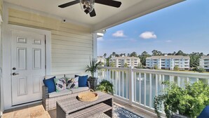 A balcony with a ceiling fan, a white door, wicker furniture, and a view of other buildings.