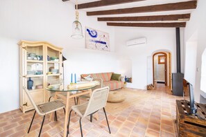 A living room with a glass table, chairs, a sofa, a cabinet with dishes, a painting, a fireplace, and a television.